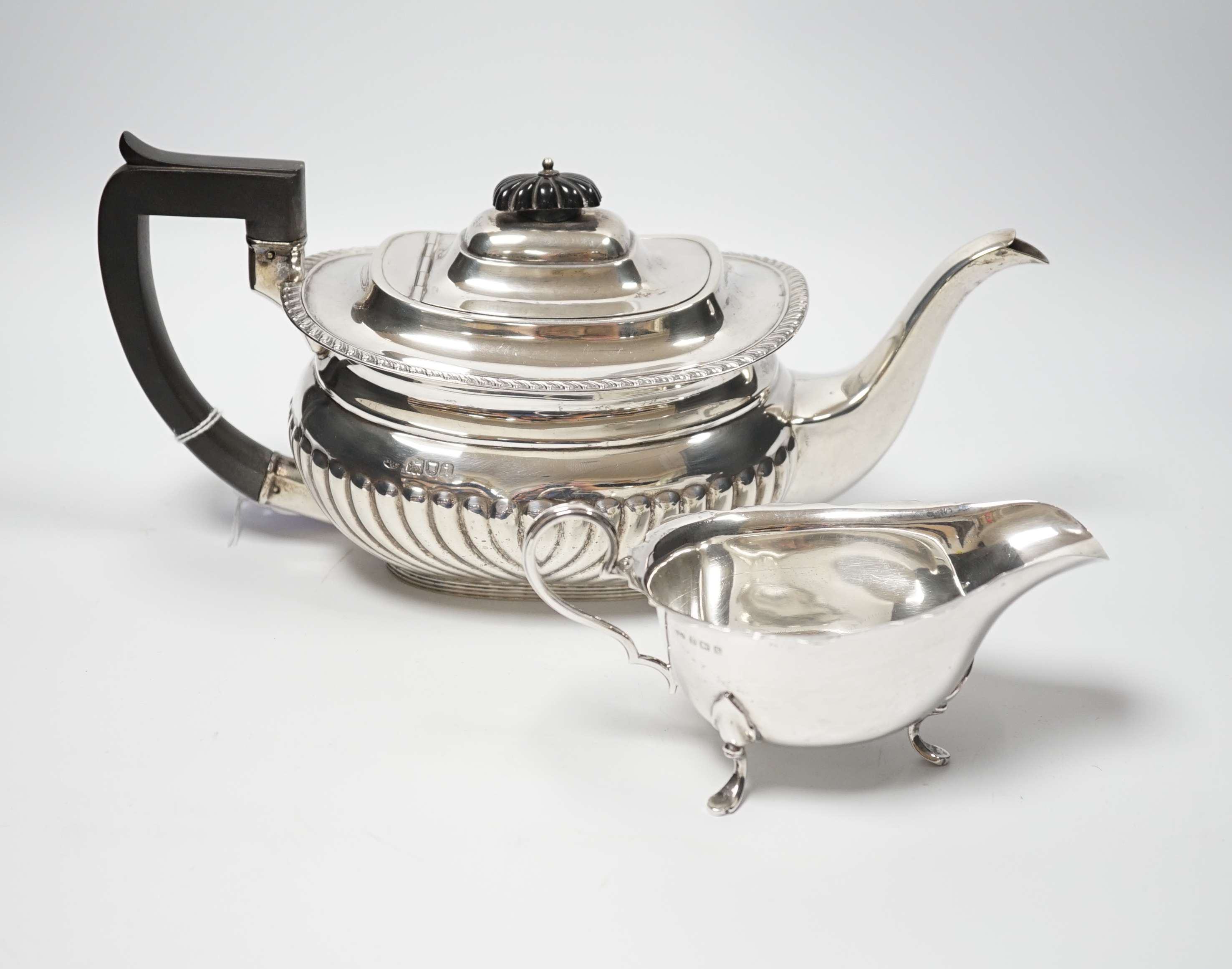 An Edwardian demi fluted silver teapot, London, 1904, together with a later silver sauceboat, gross weight 27oz.